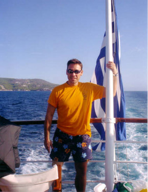 David Alonso junto a la bandera griega en un barco navegando por las islas. 